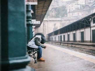 Homeless person sitting on a bench at a train station in cold weather.