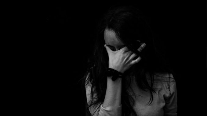 Struggling woman with head in hand, dark background, representing recovery from addiction.
