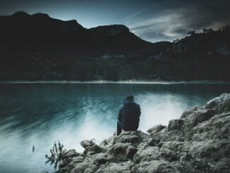 Calm person sitting by a lake at dusk, promoting sober lifestyle and mental clarity.