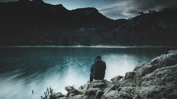 Calm person sitting by a lake at dusk, promoting sober lifestyle and mental clarity.