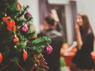 Festive Christmas tree with ornaments and decorations in focus, blurred background with two women celebrating.