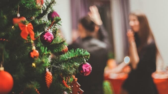 Festive Christmas tree with ornaments and decorations in focus, blurred background with two women celebrating.
