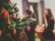 Festive Christmas tree with ornaments and decorations in focus, blurred background with two women celebrating.