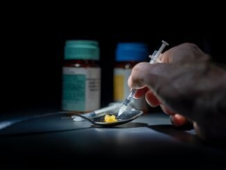 1. Close-up of hand preparing drug injection with pills and medications in a dark setting.