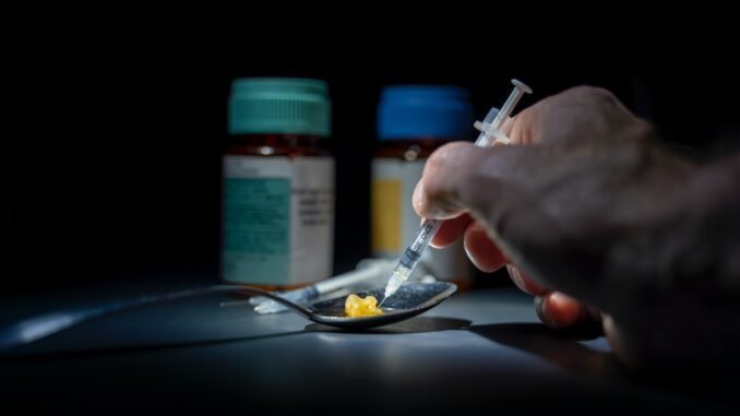 1. Close-up of hand preparing drug injection with pills and medications in a dark setting.