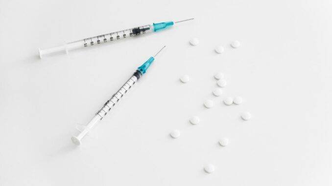 Syringe and pills on white background for substance abuse recovery and sobriety support.